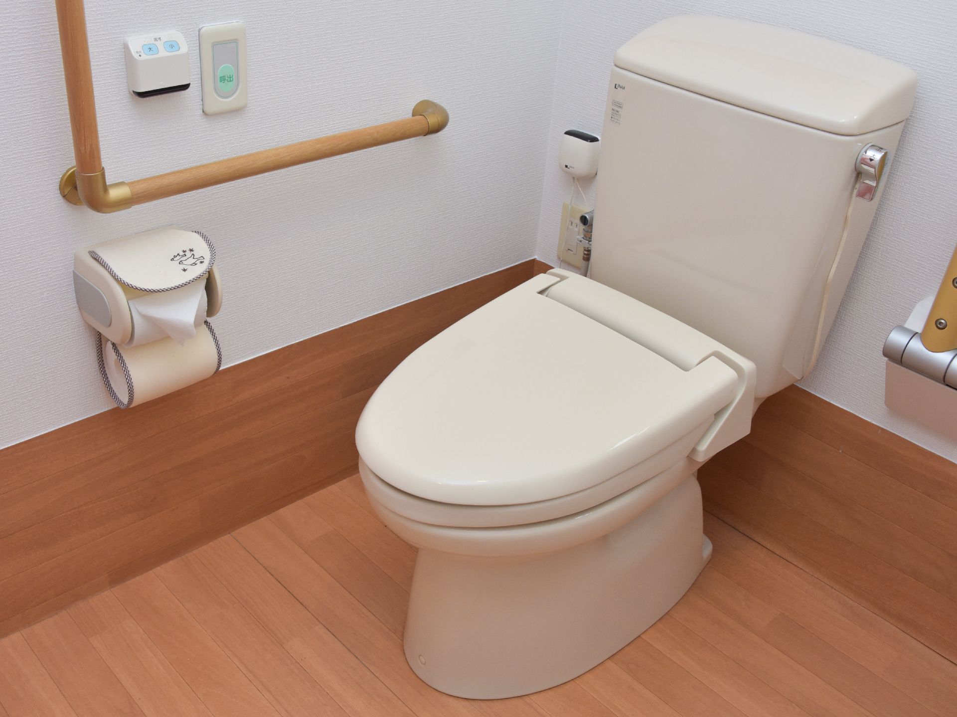 トイレはウォームレットで、両脇に手すりが設置されている。壁にはナースコールと流すボタンが付いている。