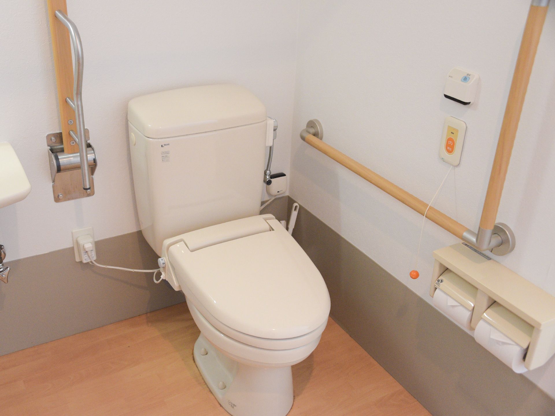 トイレにはナースコールのボタンとコールが作動する紐がついている。手すりが横と縦にわたって設置されていて、高齢者のことを考えた設計だ。