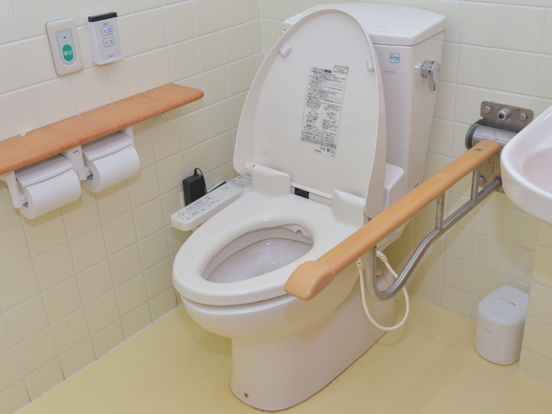 トイレには緑のボタンの呼出ベルがついている。また手すりも設置されており、高齢者の使用に配慮した設計である。