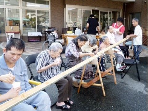 屋外で横一列に座り、流しそうめんを楽しんでいる入居者様たち