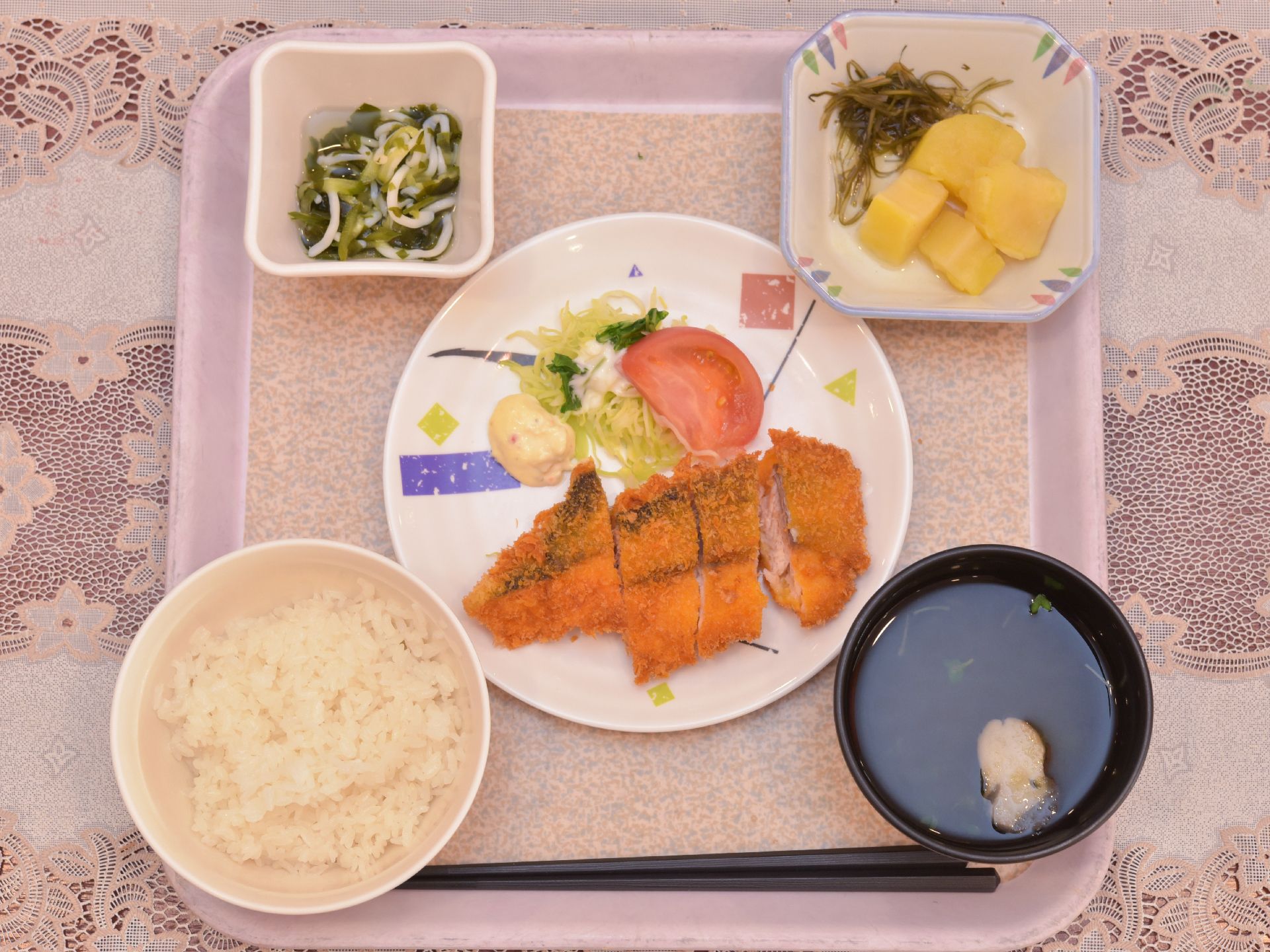 食事は、和洋折衷。器に盛られたご飯・味噌汁・お浸し・サラダ・魚のフライ・お漬物がおぼんの上に並んでいる。