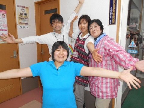 笑顔で両手を広げてポーズをとっている、4名のスタッフ