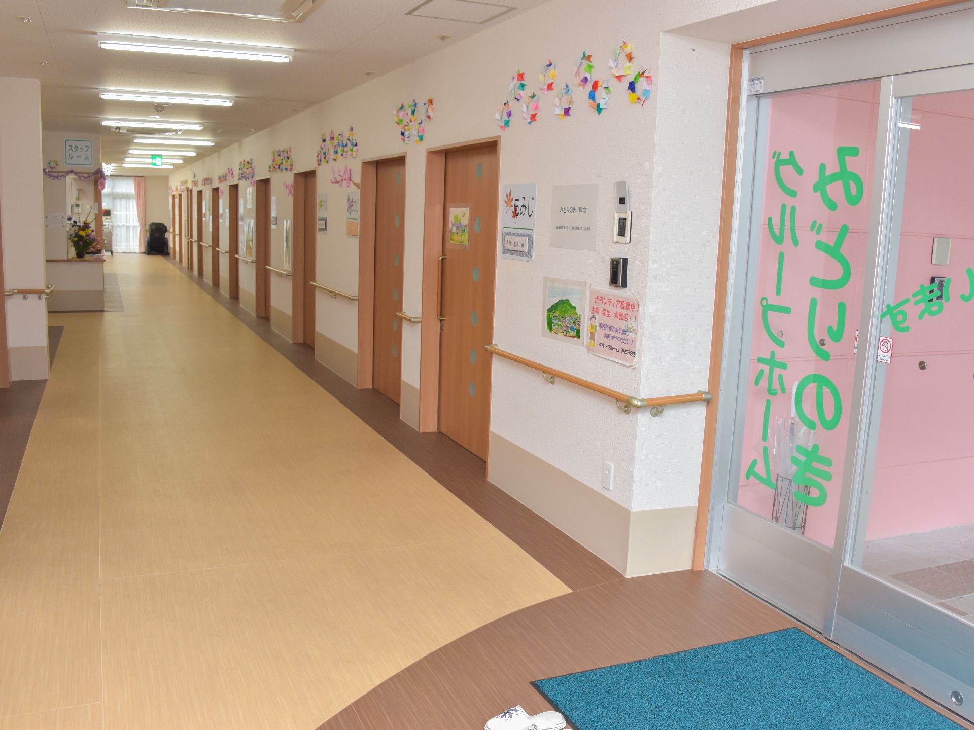 廊下は、ベージュと茶色のデザインの床には段差がなく、安全に通行出来る。手作りの飾りつけが明るい雰囲気を演出している。