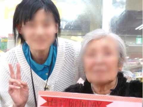 HAPPYBIRTHDAYと書かれたボードを持ち、笑顔でスタッフと並んでいる女性