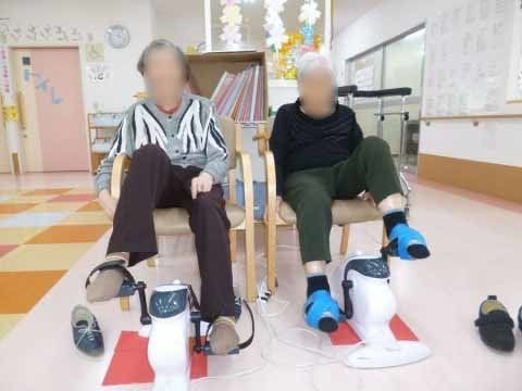 手すり付きの椅子に座り、機器を使って足の運動をしている二名の入居者様