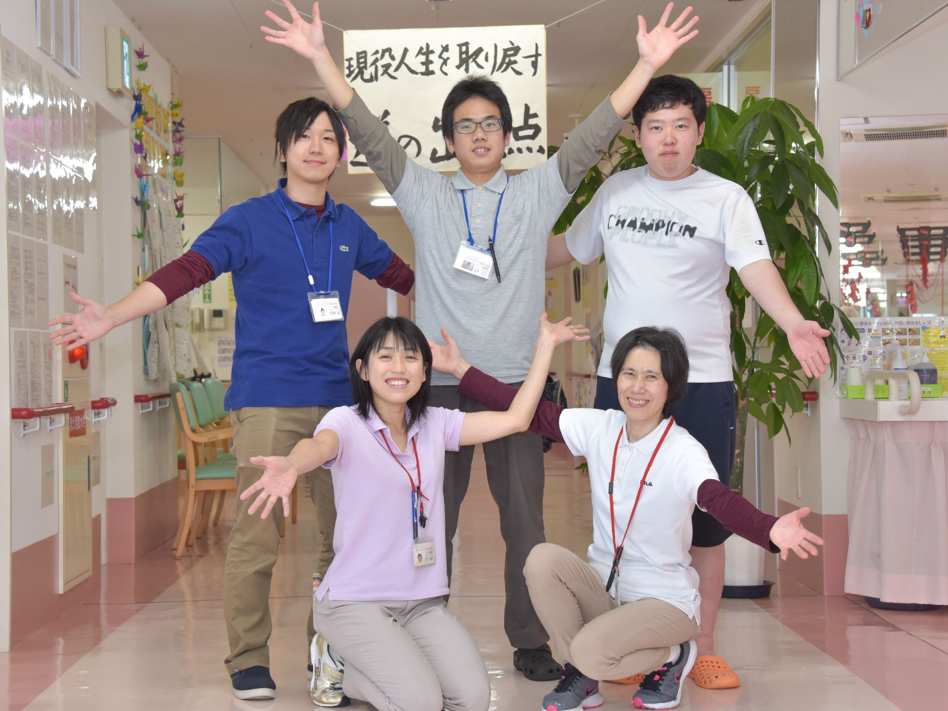 廊下に飾られた標語の前で、ポーズをとっている五名のスタッフたち