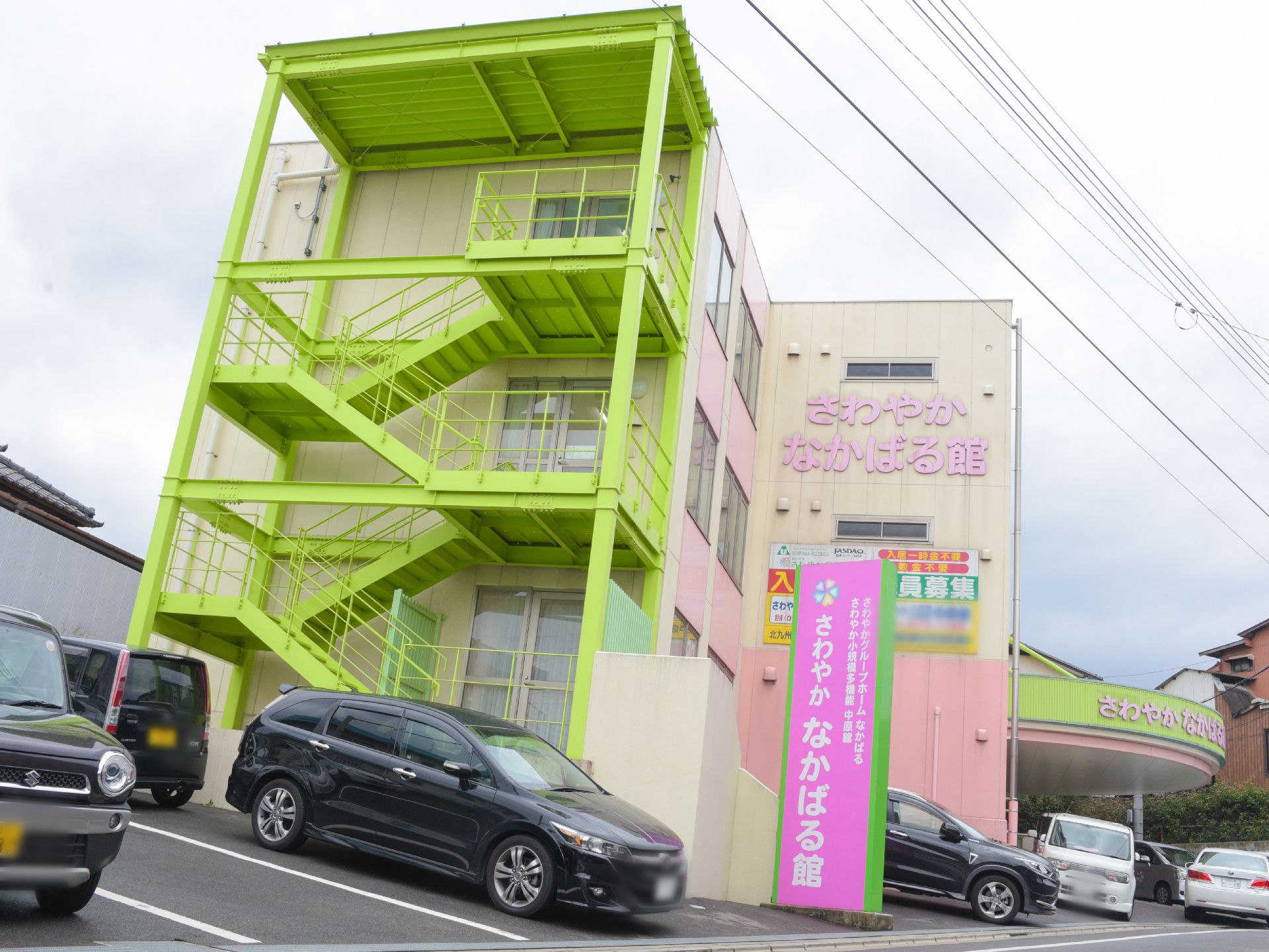 黄緑色に塗られた外階段が設置されている、パステルカラーの施設外観