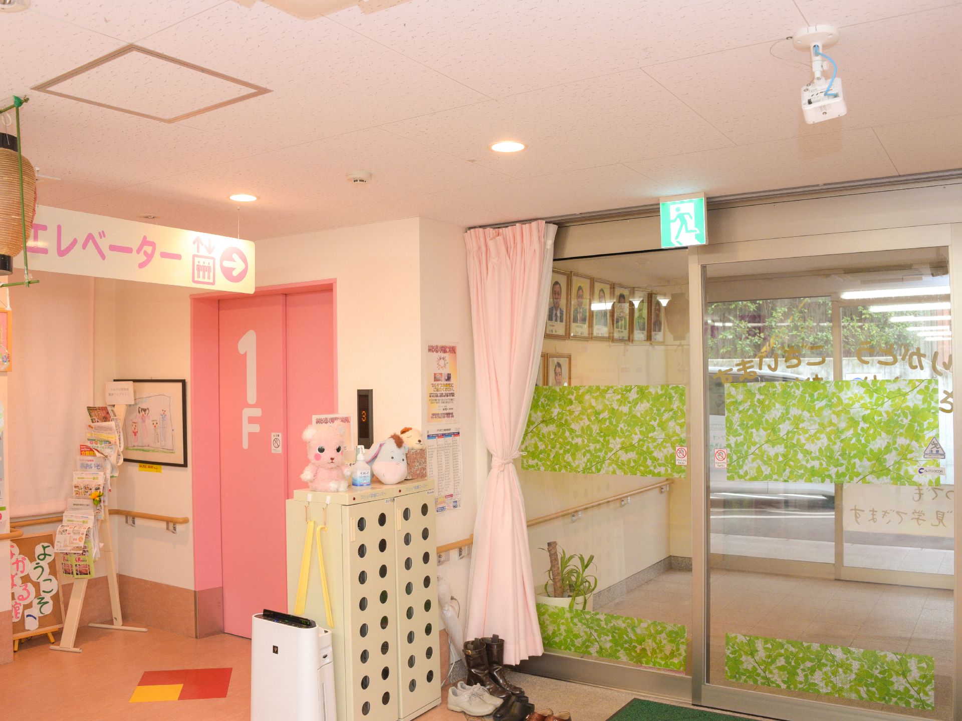 入口は、二重の自動扉となっている。表示やカーテン、エレベーター等、ピンクの温かみのあるデザインで統一されている。