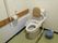 トイレの両側には可動式の手すりがあり、背面には背当て用のパッドが設置されている。壁にはナースコールのボタンと紐がある。