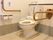 白色基調のトイレスペース。便器の両側には、茶色の手すりが設置されている。壁にはナースコールが取り付けてある。