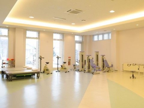 窓際に数種類のリハビリテーション機器が設置されている、広々としたリハビリルーム