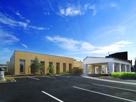 手前に広い駐車スペースがあり、奥に黄土色と白色の建物がある風景