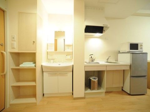 部屋の中には収納スペース、洗面台、ミニキッチンが用意されている。白い壁に床はフローリングの部屋である。