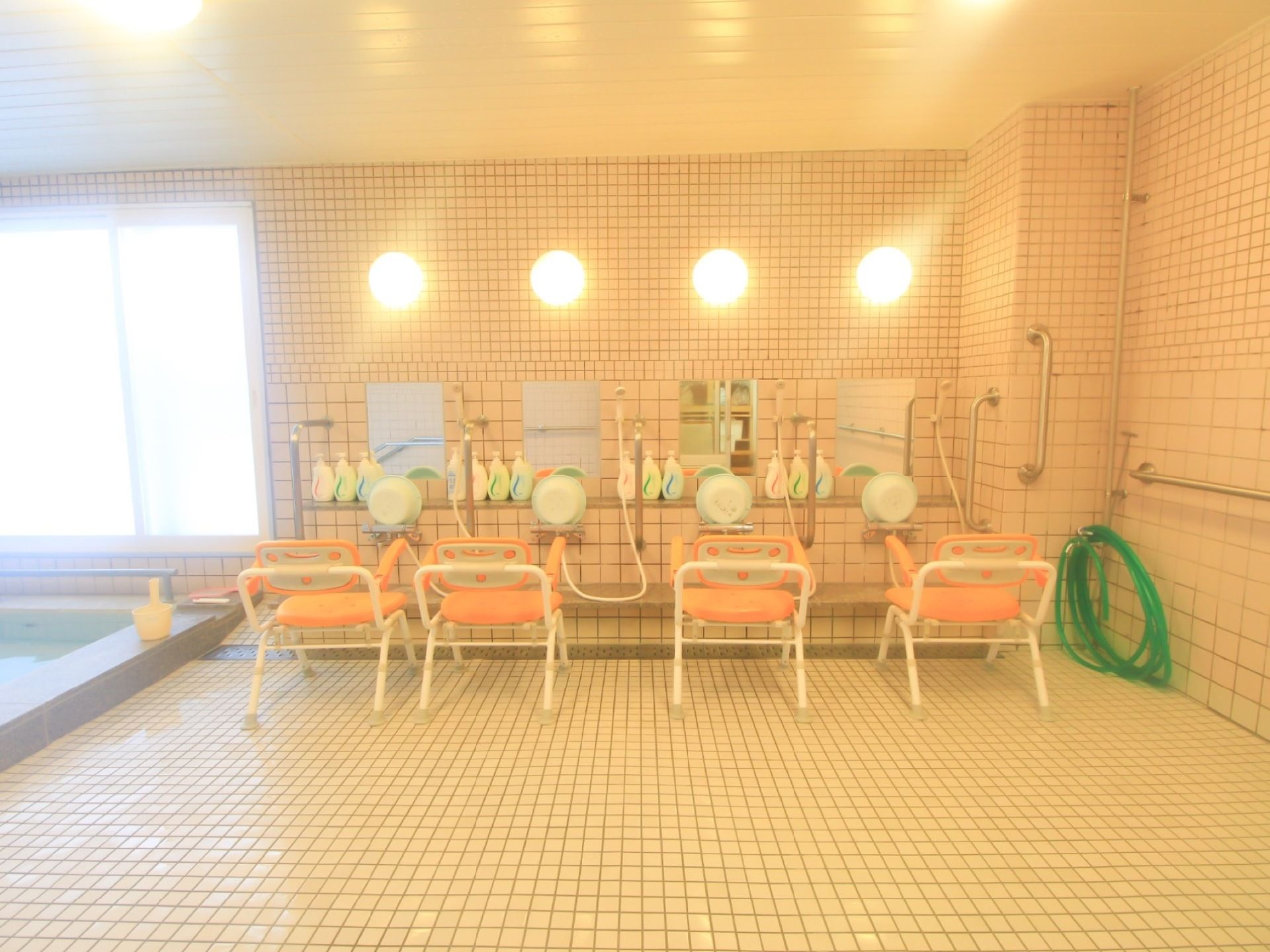 広々とした大浴場の洗い場である。壁には手すりや鏡、椅子、桶などが用意されており、同時に４人が利用できるようになっている。
