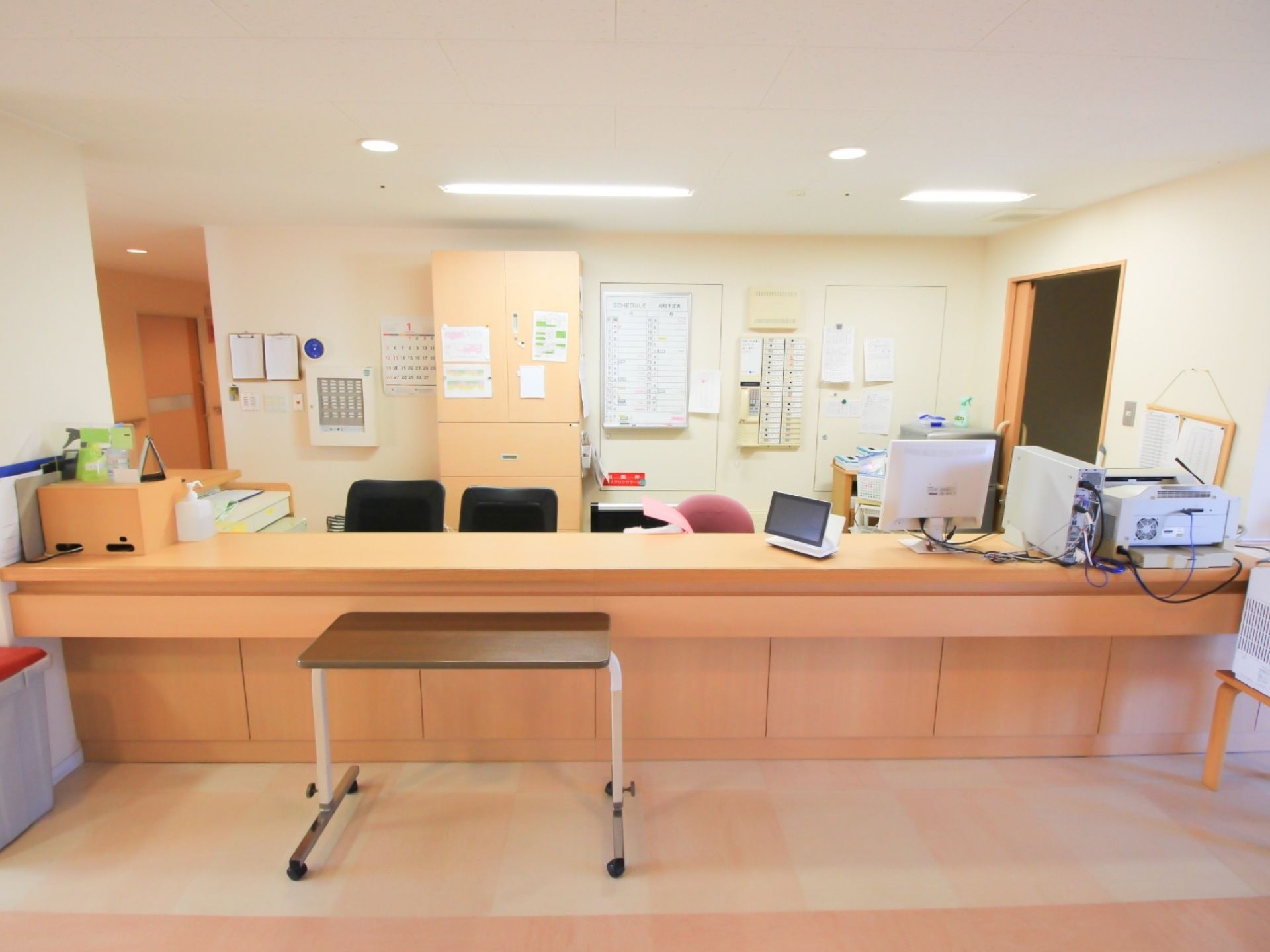 施設内の通路沿いにスタッフステーションが設置されている。テーブルや椅子、パソコンのほか、壁には予定表やカレンダーが掛けられている。