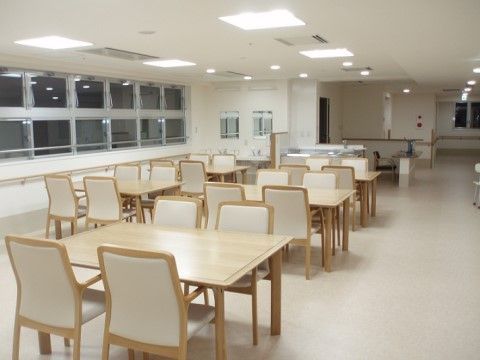 居室はゆったりとした広さが確保されており、白い椅子と木目調のテーブルがたくさん用意されている。部屋の隅には、洗面台もある。