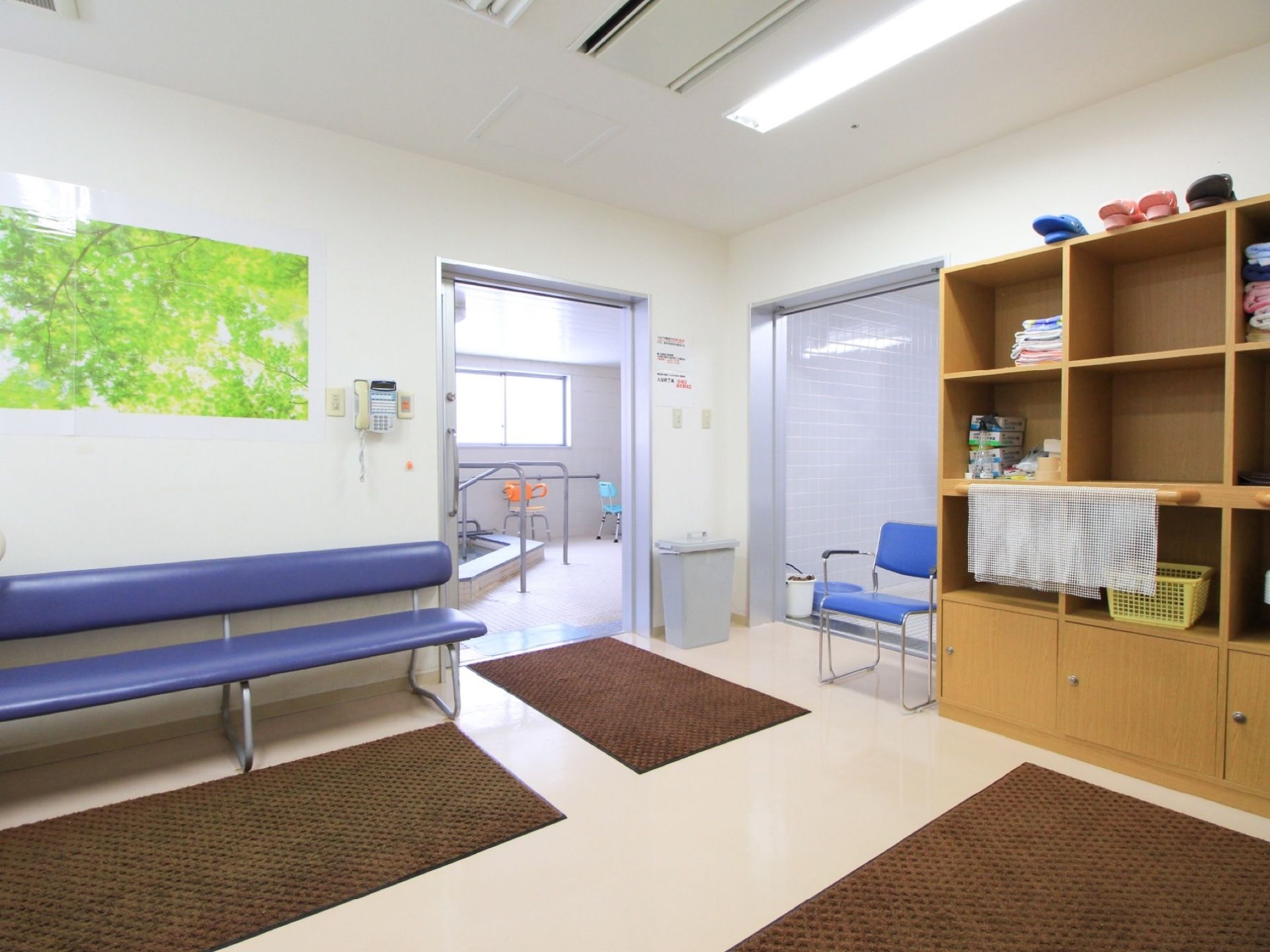クリーム色の床の上に３枚の茶色いマットが敷いてある。背もたれ付きの青いベンチと大きな収納棚が置いてある。