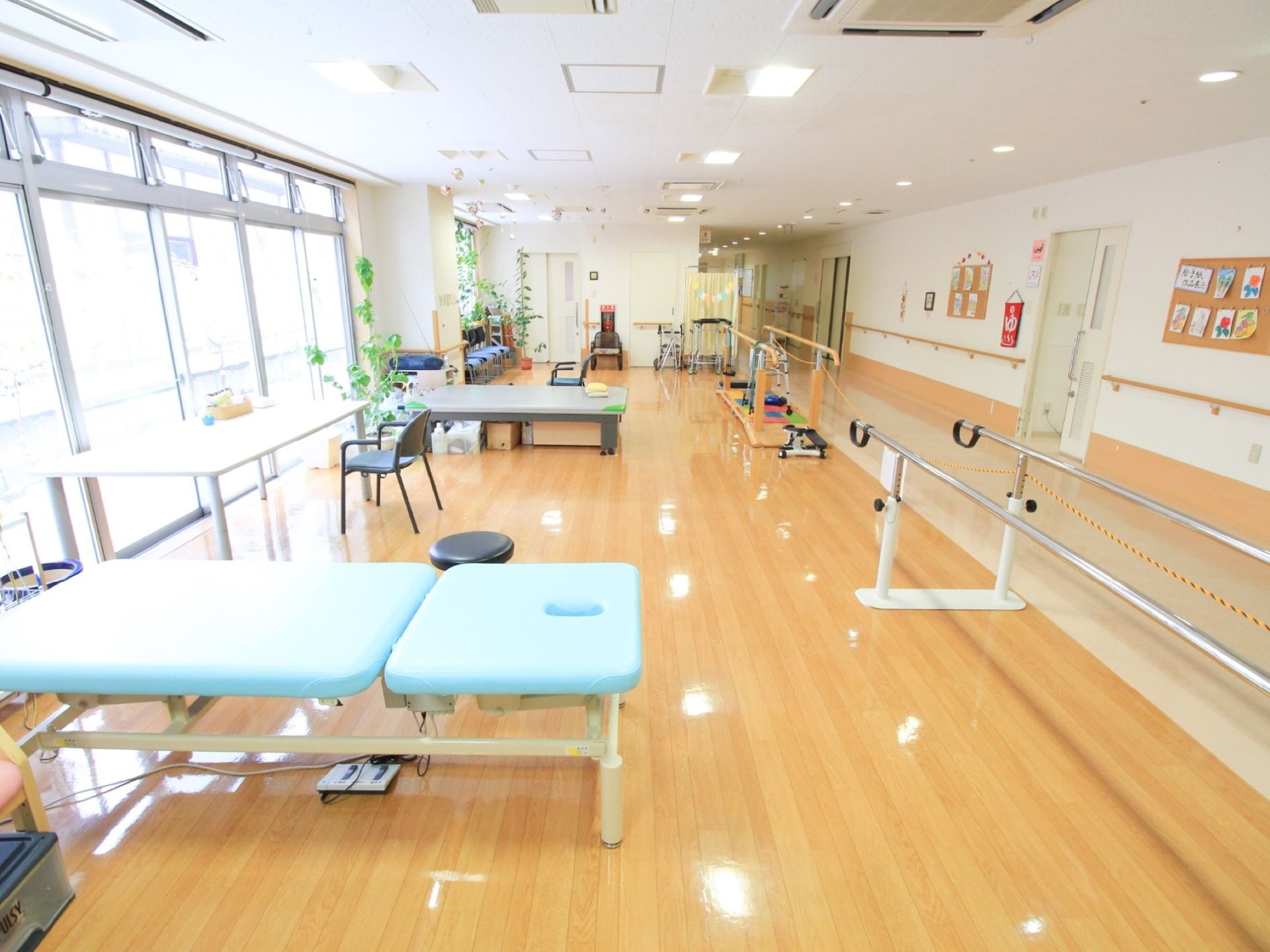 ピカピカに磨かれたフローリングの床の部屋がある。水色のマットレスの台や平行棒などの器具がたくさんある。