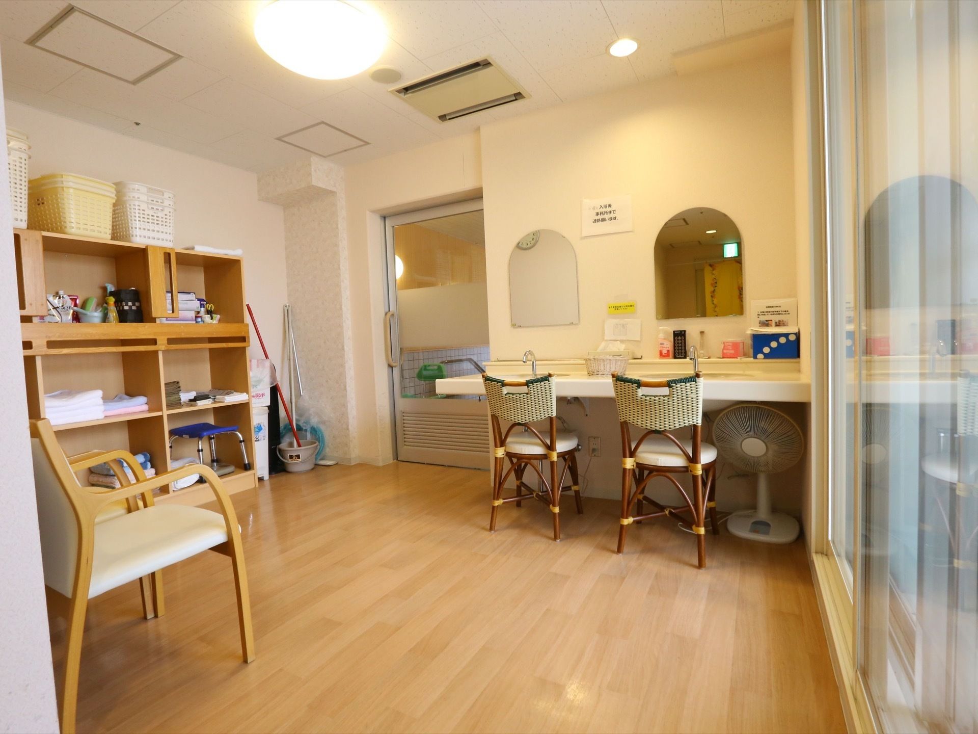 大浴場前の脱衣室には、洗面台と鏡が２つずつある。椅子４脚のほかに、脱衣かご、タオル、大浴場の掃除用具などが置かれている。