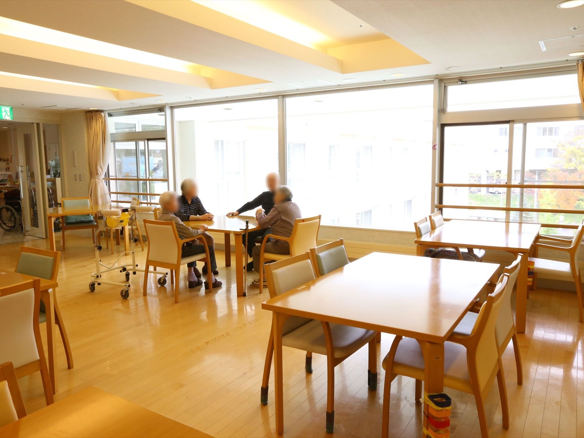 食堂に、多くのテーブルと椅子が置かれている。天井の照明は、掘り込み式の間接照明になっている。大きな窓がある。