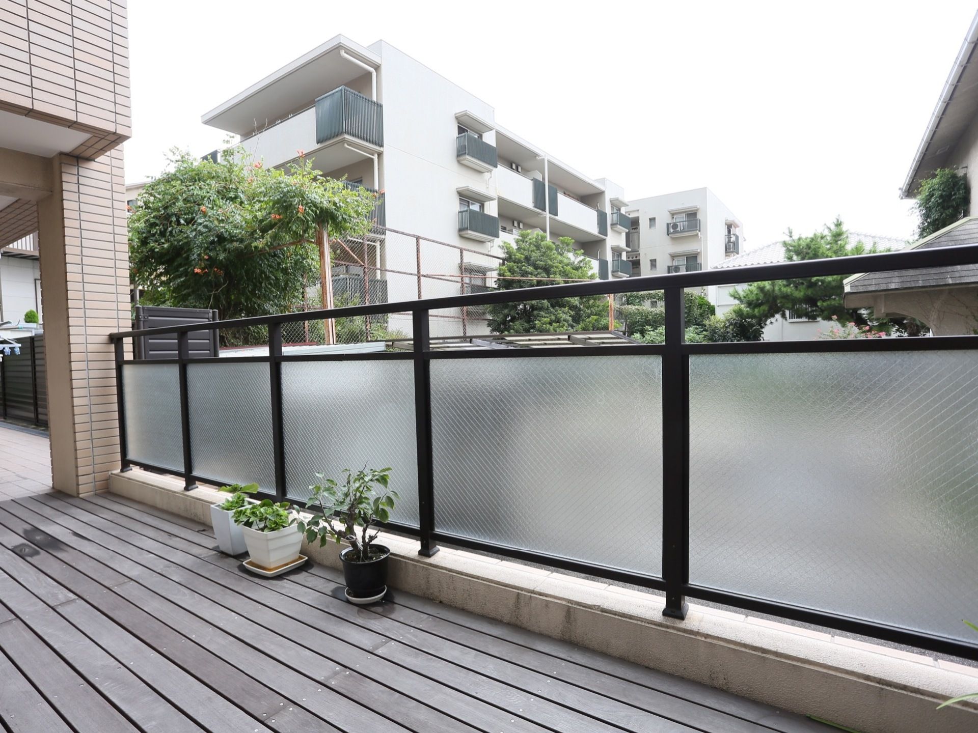 お部屋の外に設けたウッドデッキである。すりガラスのフェンスを設置し、床に小さめの緑の植木鉢を並べて飾っている。