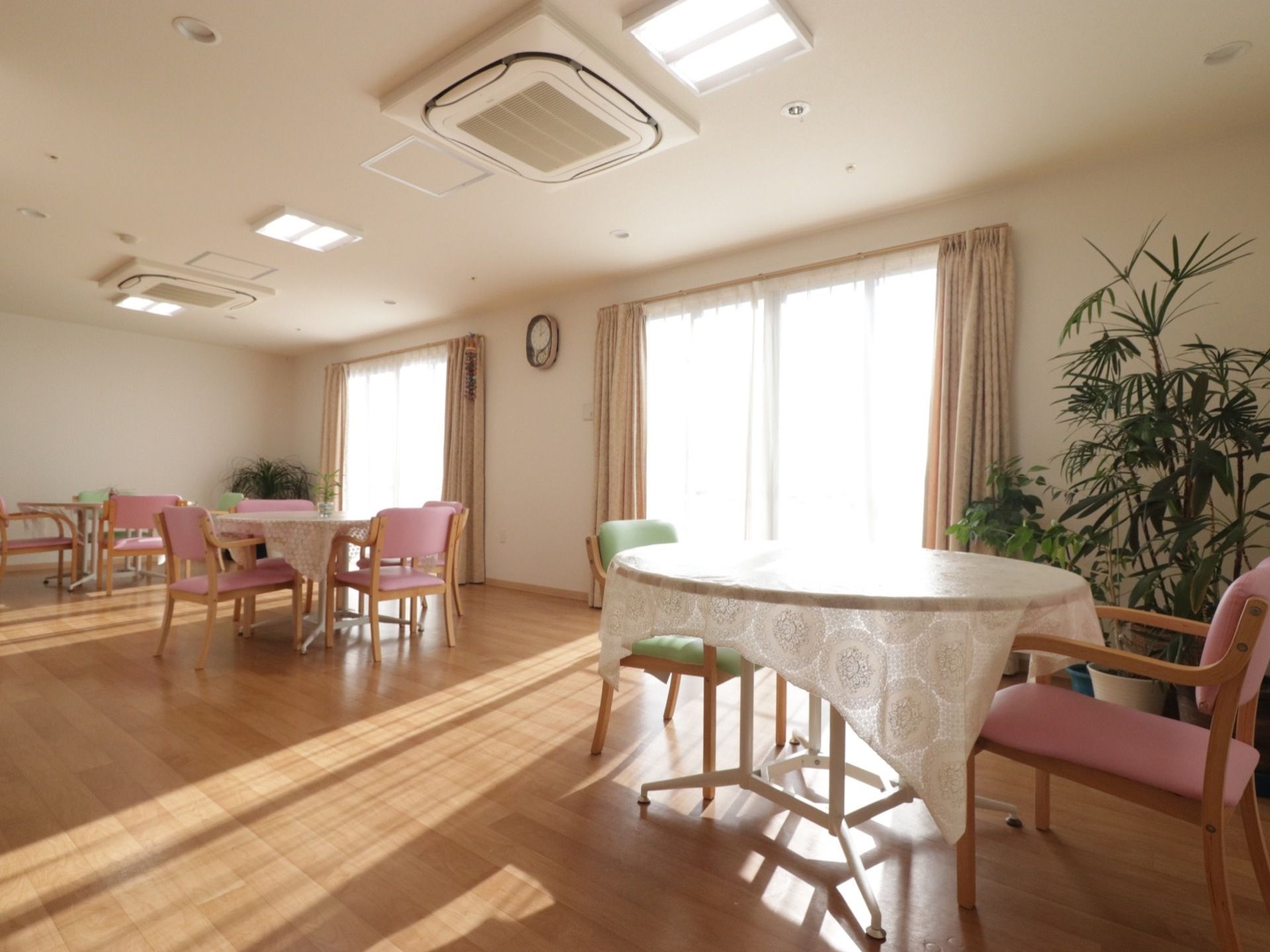 ２つの窓から明るい日差しが差し込んでいる。丸いテーブルが３カ所に置かれている。天井にはエアコンが２つ設置されている。
