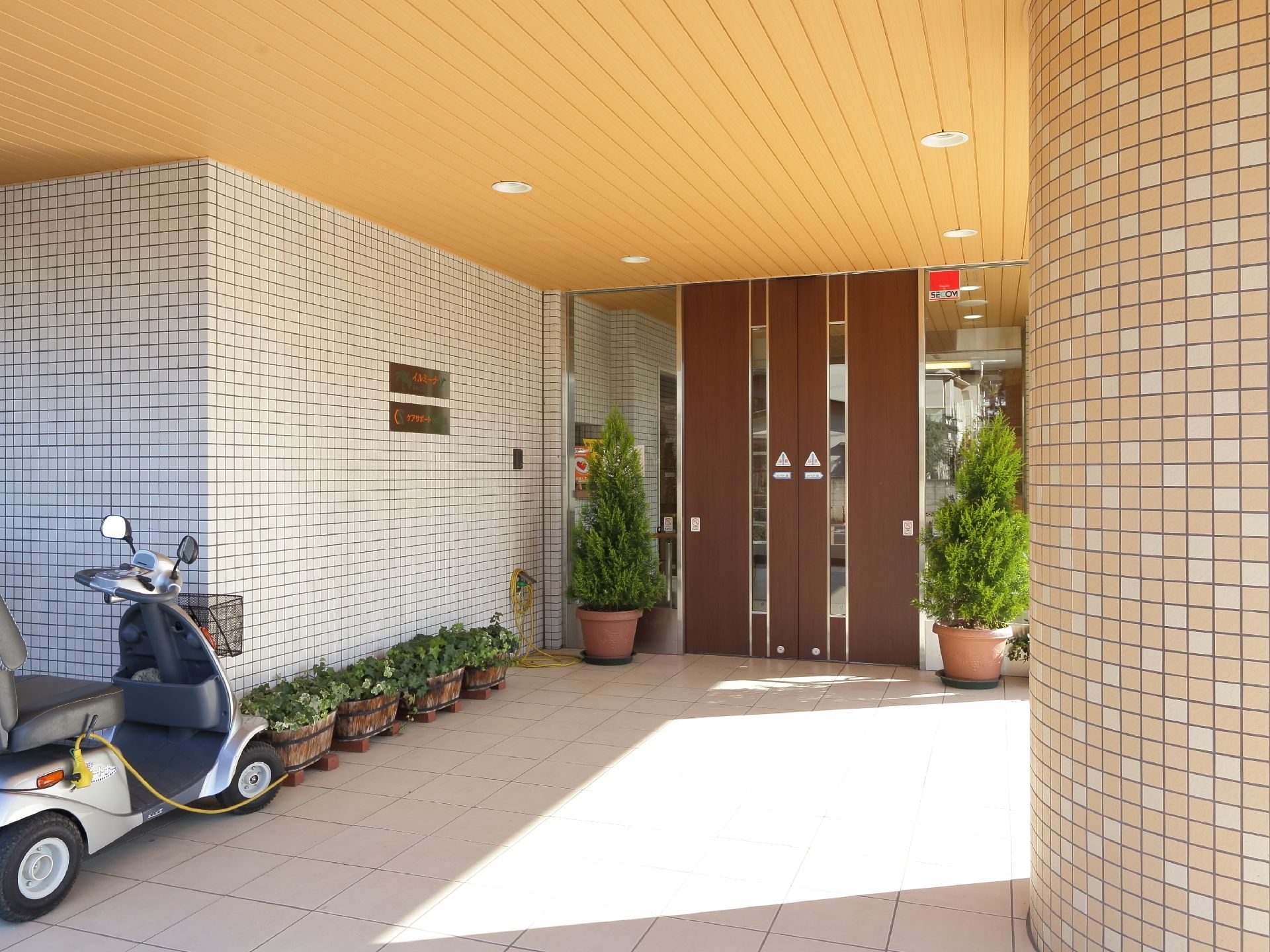 ご利用者をお迎えする正面玄関。多くの植栽を置き、グリーンがもたらす心の安らぎを感じさせている。雨除けは幅広く取り、降雨時に対応。