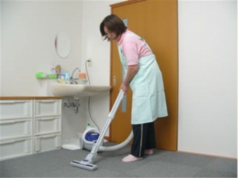 エプロンを付けて、洗面台周辺に掃除機をかけている女性スタッフ