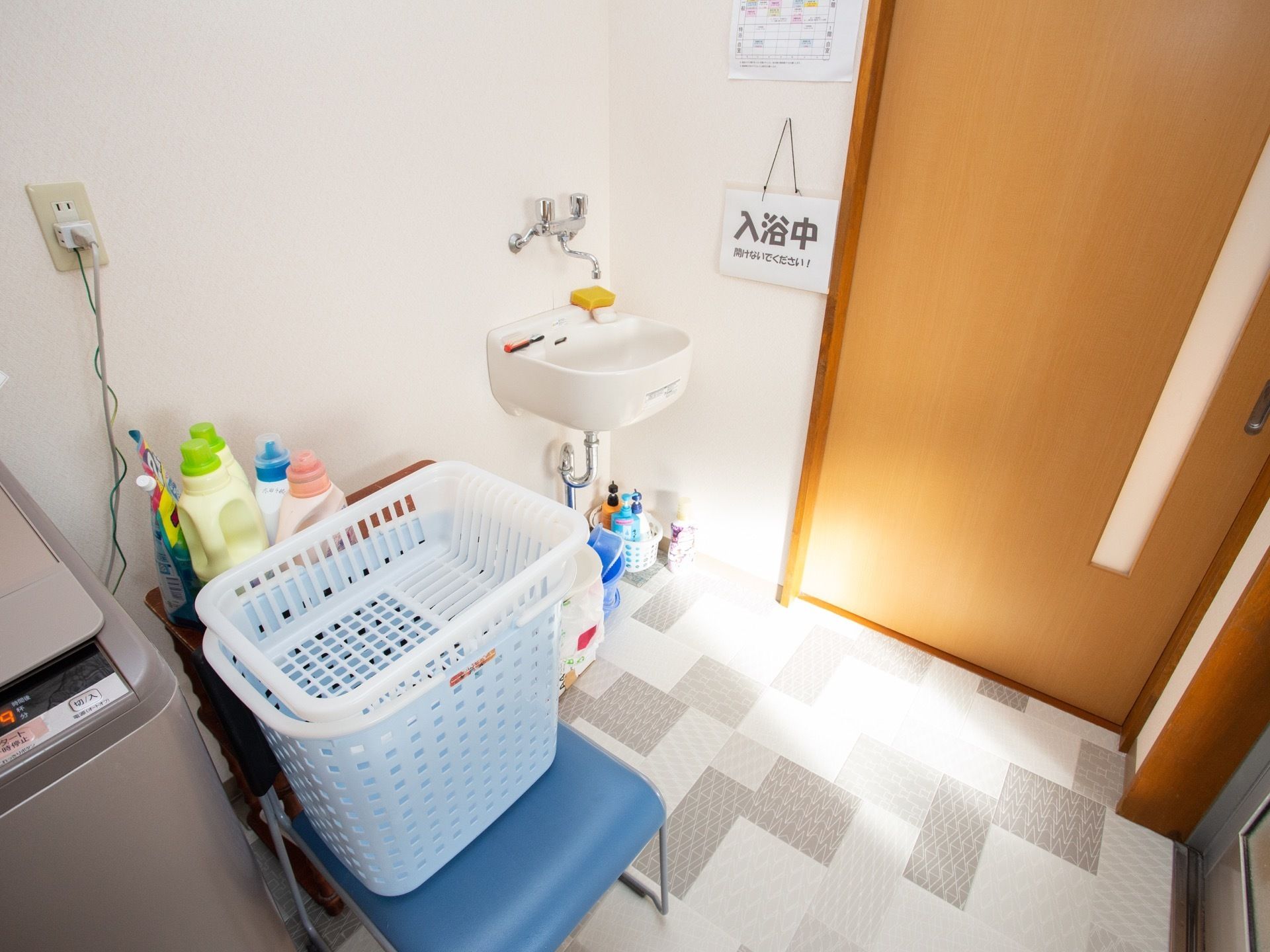 脱衣所には、洗濯機や洗剤が置いてある。浴室のドアには、入浴中であることを示す札が用意されている。服を入れるカゴもある。