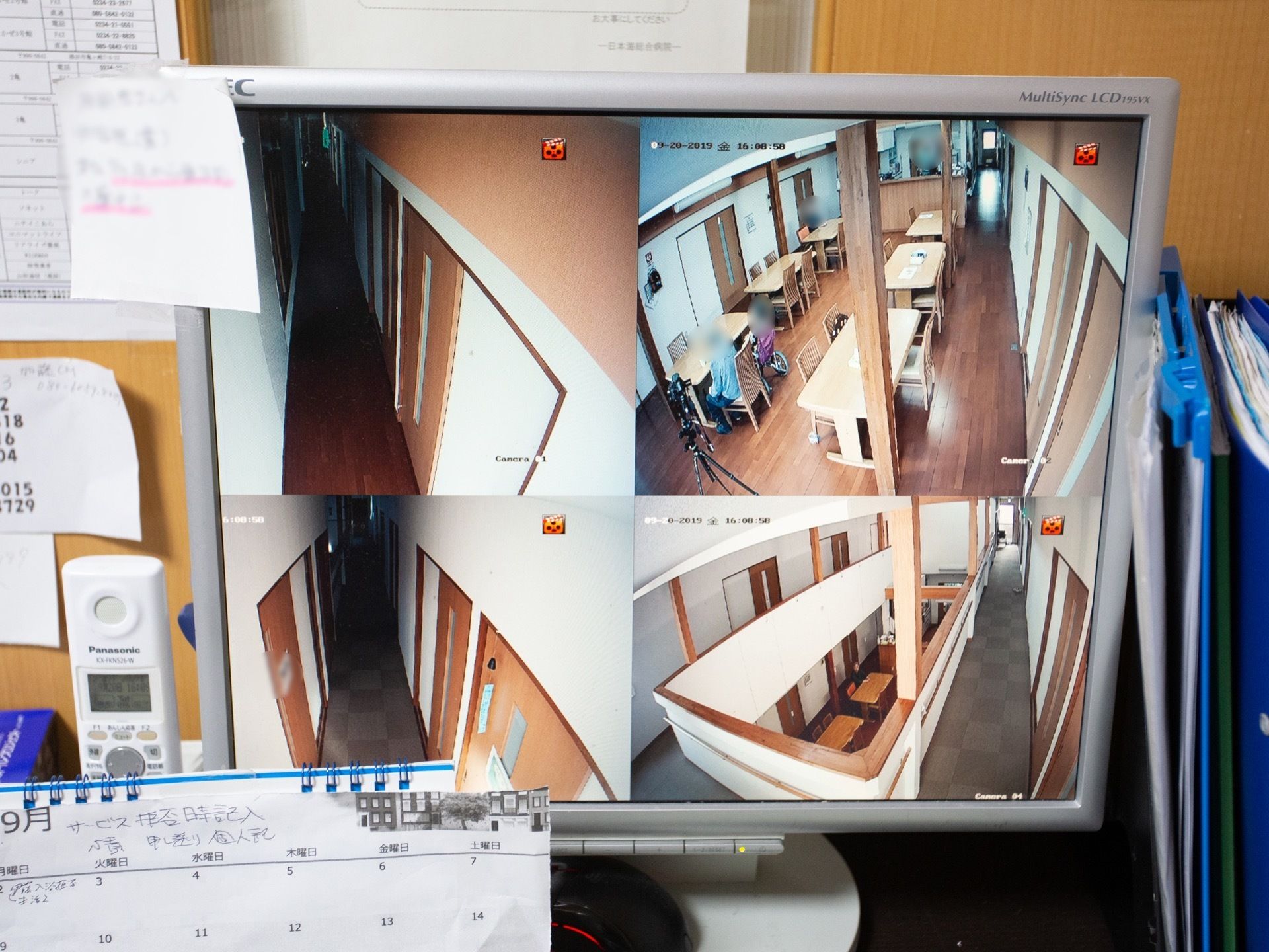 事務室にはディスクトップパソコンが置かれており、室内のモニターが映されている。卓上カレンダーが用意されている。