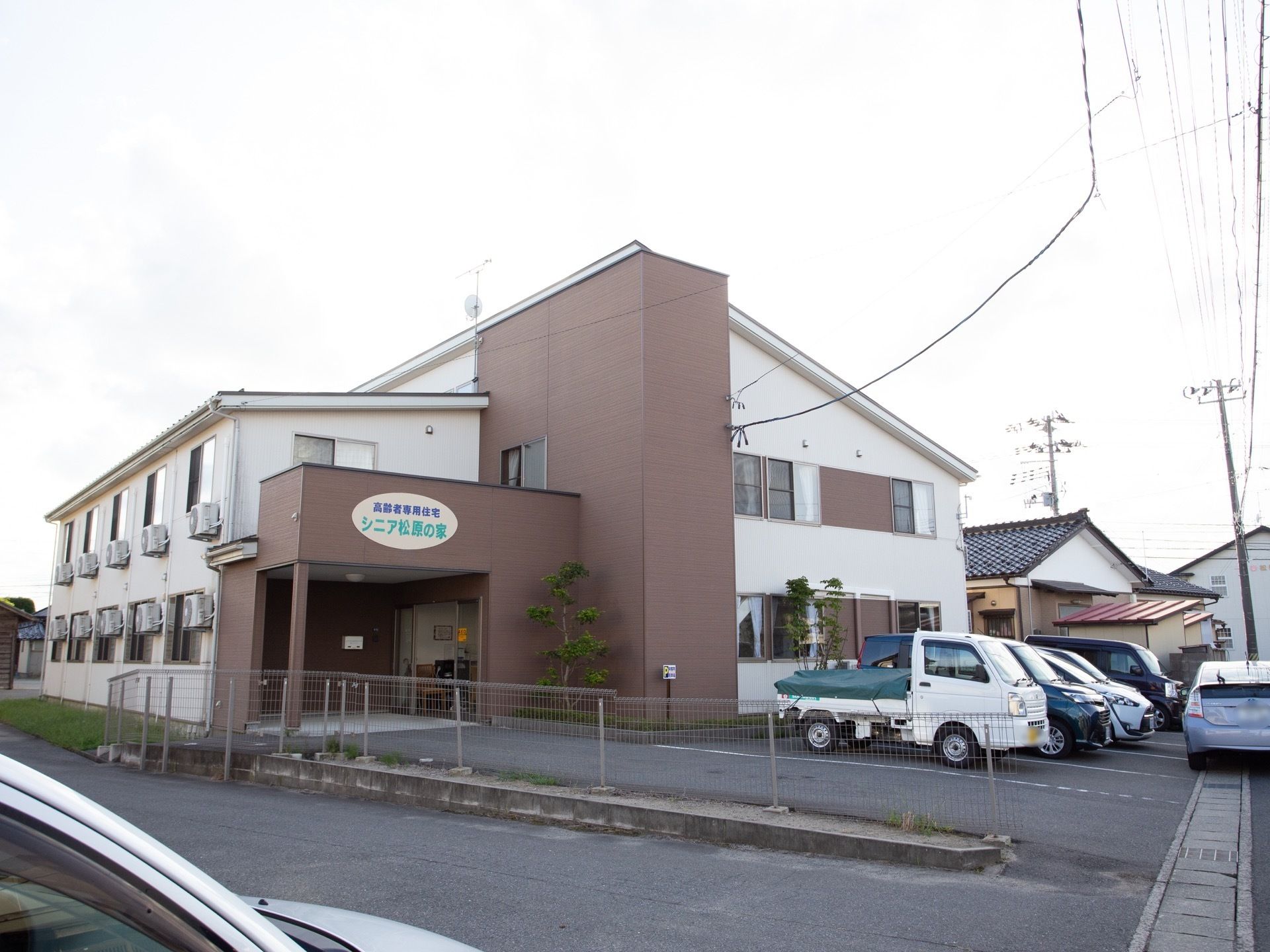 白と茶色を基調とした施設外観である。２階建ての建物になっており、外壁には施設名が記された看板が設置されている。