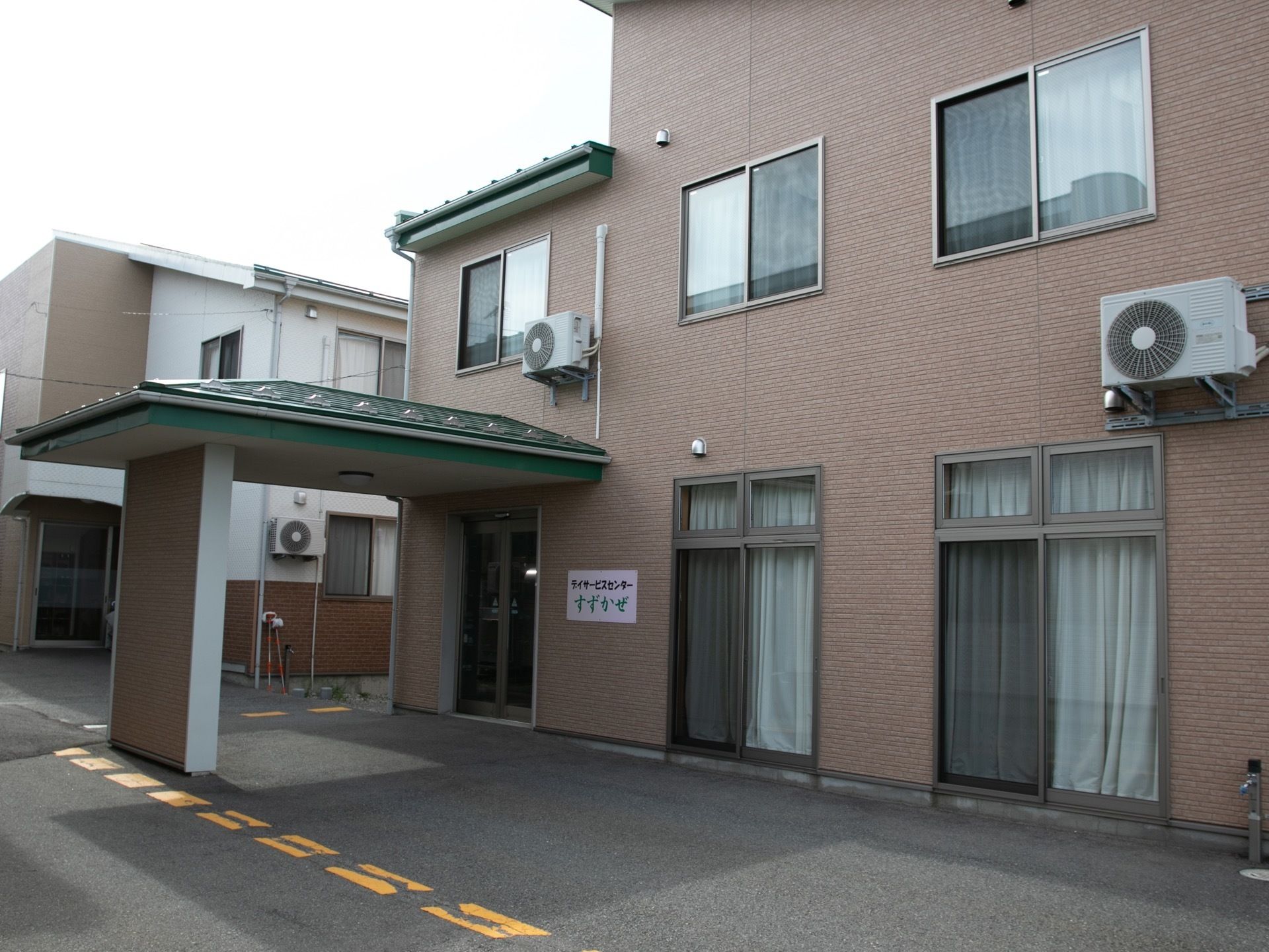 舗装された敷地に、２階建ての住宅が建っている。入り口は自動ドアで屋根が付けられている。