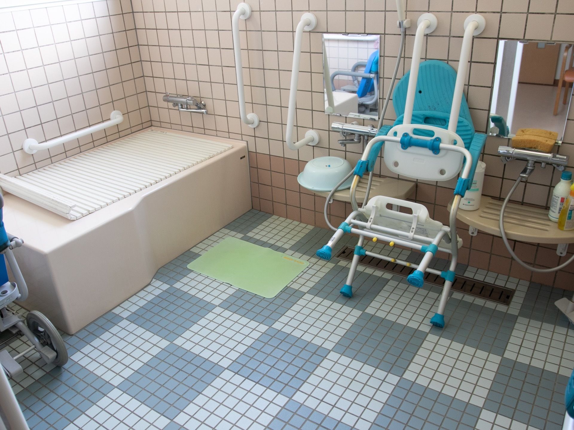 白と青のタイルが張られた広い浴室がある。洗い場には入浴用の椅子が置かれ、シャワーや浴槽のまわりには手すりがある。