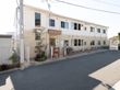 2階建ての建物で、1階と2階で異なる色の外壁が使用されている。敷地内の端に自販機が1台設置されている。