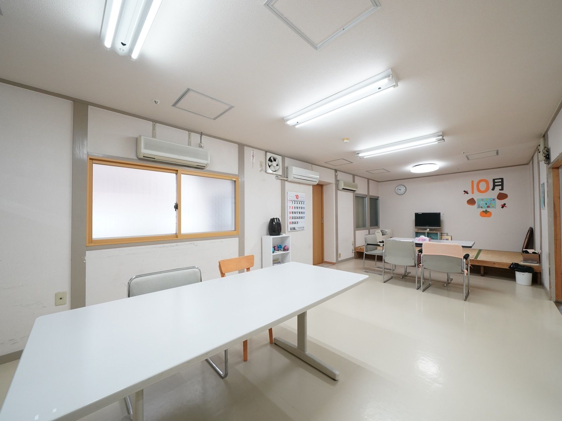 白いエアコンが天井近くに２台設置されている。壁には、絵画や手作りの掲示物が飾られており、明るい雰囲気である。