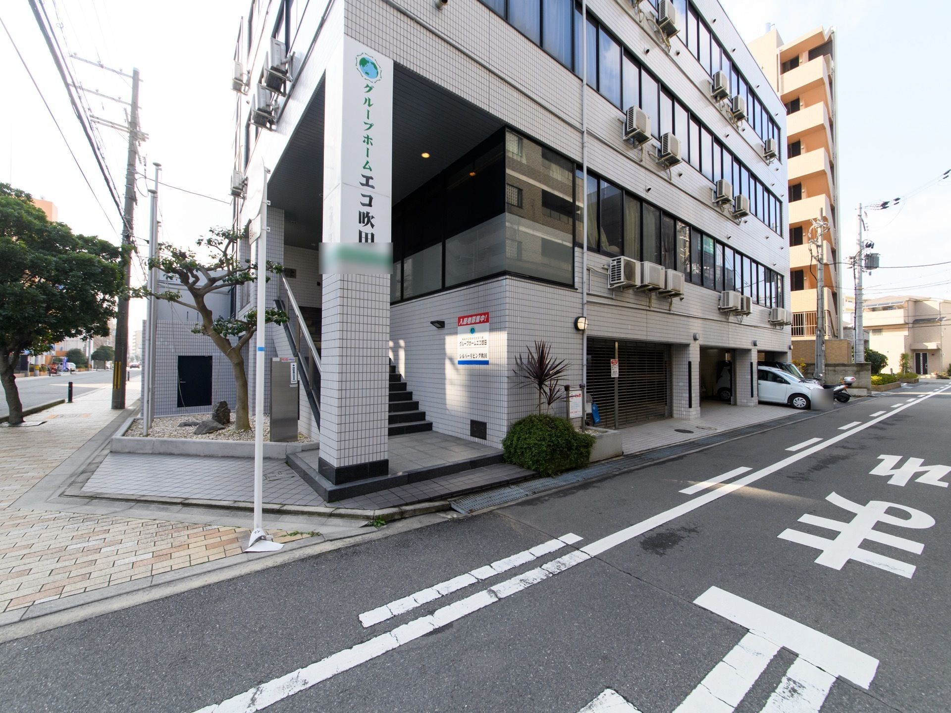 施設はタイル張りの4階建ての建物。2階が入口になっている。角地にあり、隣接する道路には広めの歩道がある。