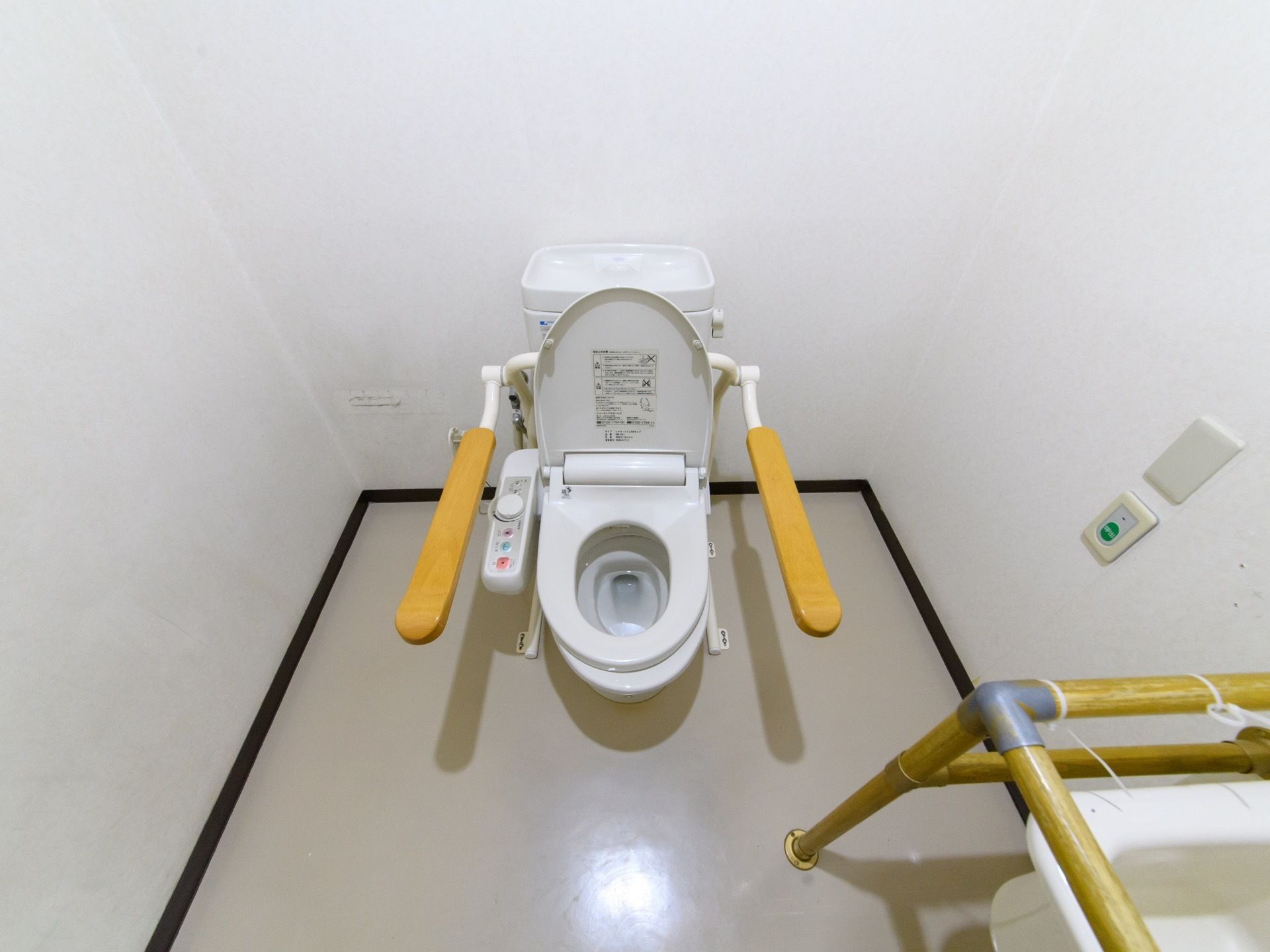 温水洗浄便座が付いた洋式トイレが設置されている。左右には手すりが追加されている。壁にはナースコールが付いている。