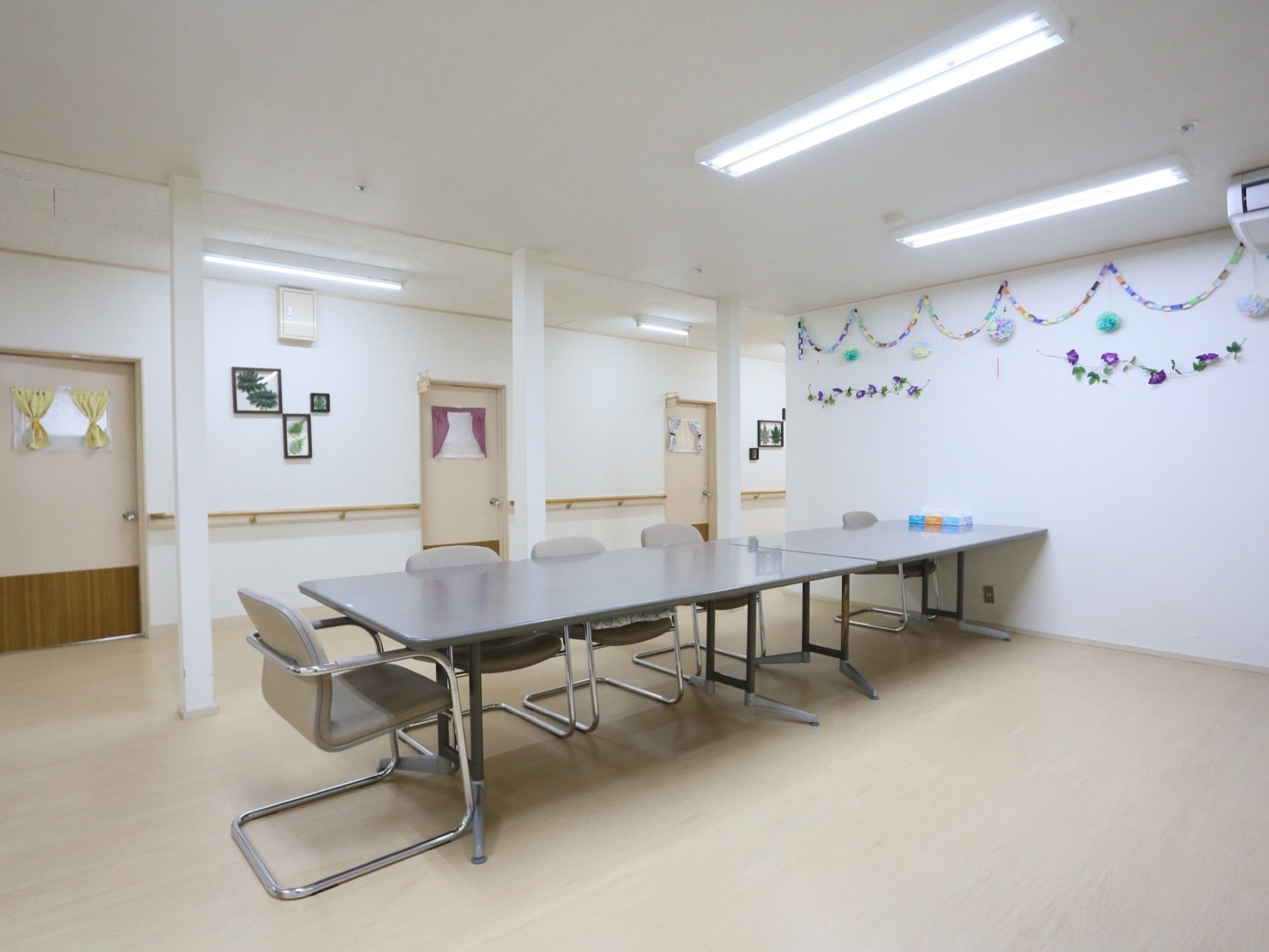入居者様が作業しやすいよう大きな長机と椅子があり、壁には色とりどりの紙で作ったリースが飾られている。