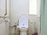 真っ白な温水洗浄便座が備えつけられたトイレである。便座の両側に手すりを完備。壁側にも縦、横型の手すりが設置されている。