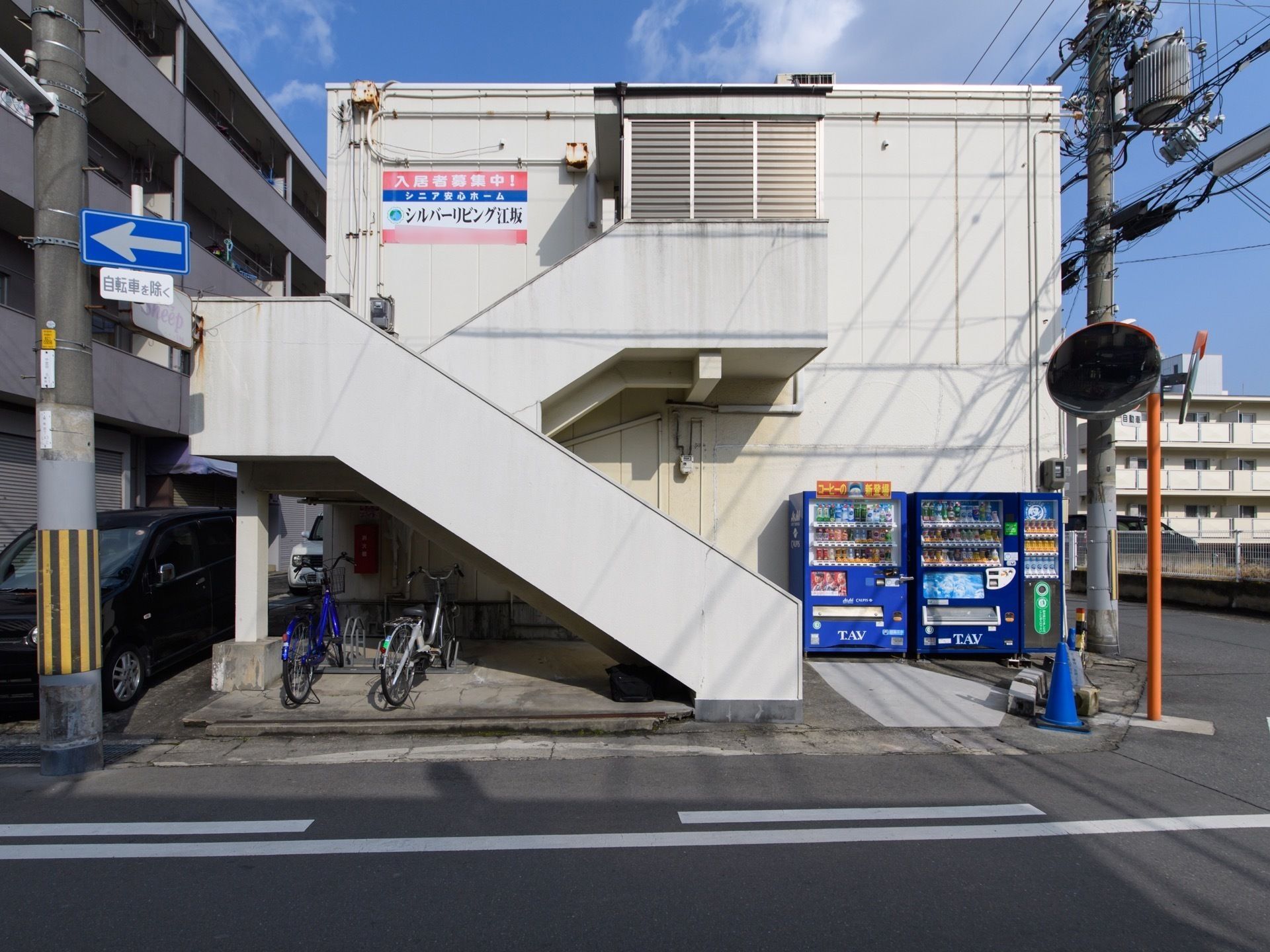 グループホームは、２階建ての建物になっている。階段の下には駐輪場があり、敷地内には自動販売機が置かれている。
