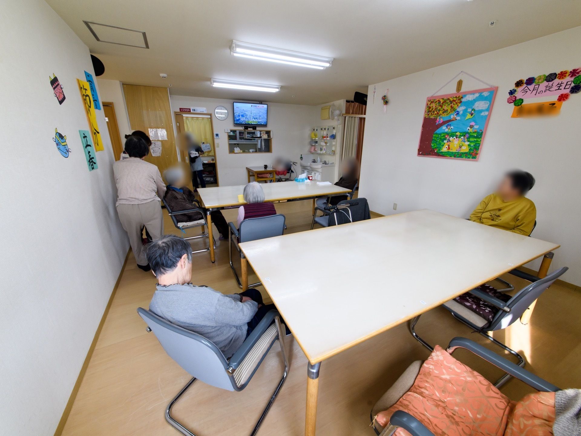 共有スペースの壁には、手作りのポップや入居者様の作品が飾られている。また奥にはテレビも備え付けている。