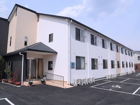 玄関前に黒色のルーフが付いている、ホワイト色の壁をした二階建て施設