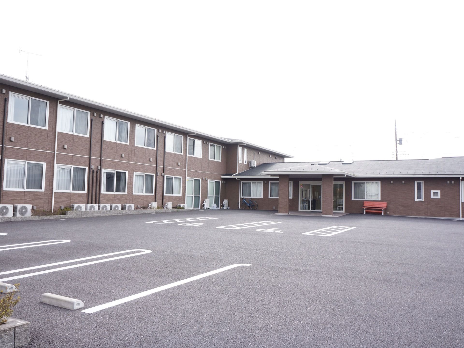 2階建てのダークブラウンの外壁でシックな雰囲気になっている。広々とした駐車場を施設の前に確保している。