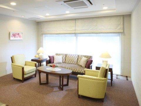 楕円形のテーブルの周りに３人掛けのソファーが１脚と、１人掛けの２脚のソファーが置いてある。窓にプレーンシェードのカーテンが掛けられている。
