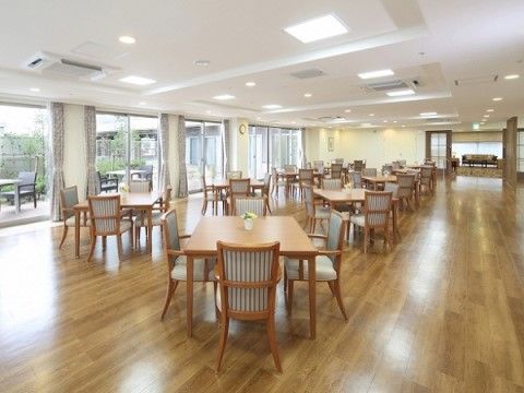 木目のフローリングの床の広々とした空間に、たくさんの４人掛けのダイニングセットが並べられている。数か所の大きな窓から外のテラスが見える。