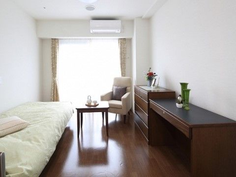 居室は茶色と白色でまとめられた落ち着いた空間になっている。ベッドやテーブル、ソファ、タンス、エアコンが完備されている。