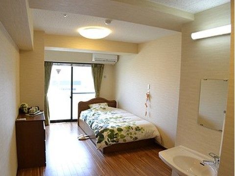 温かみがある木材の床で、ベッドとタンスが居室に置かれている。洋風の個室となっており、布団やカーテンが緑色で統一されている。
