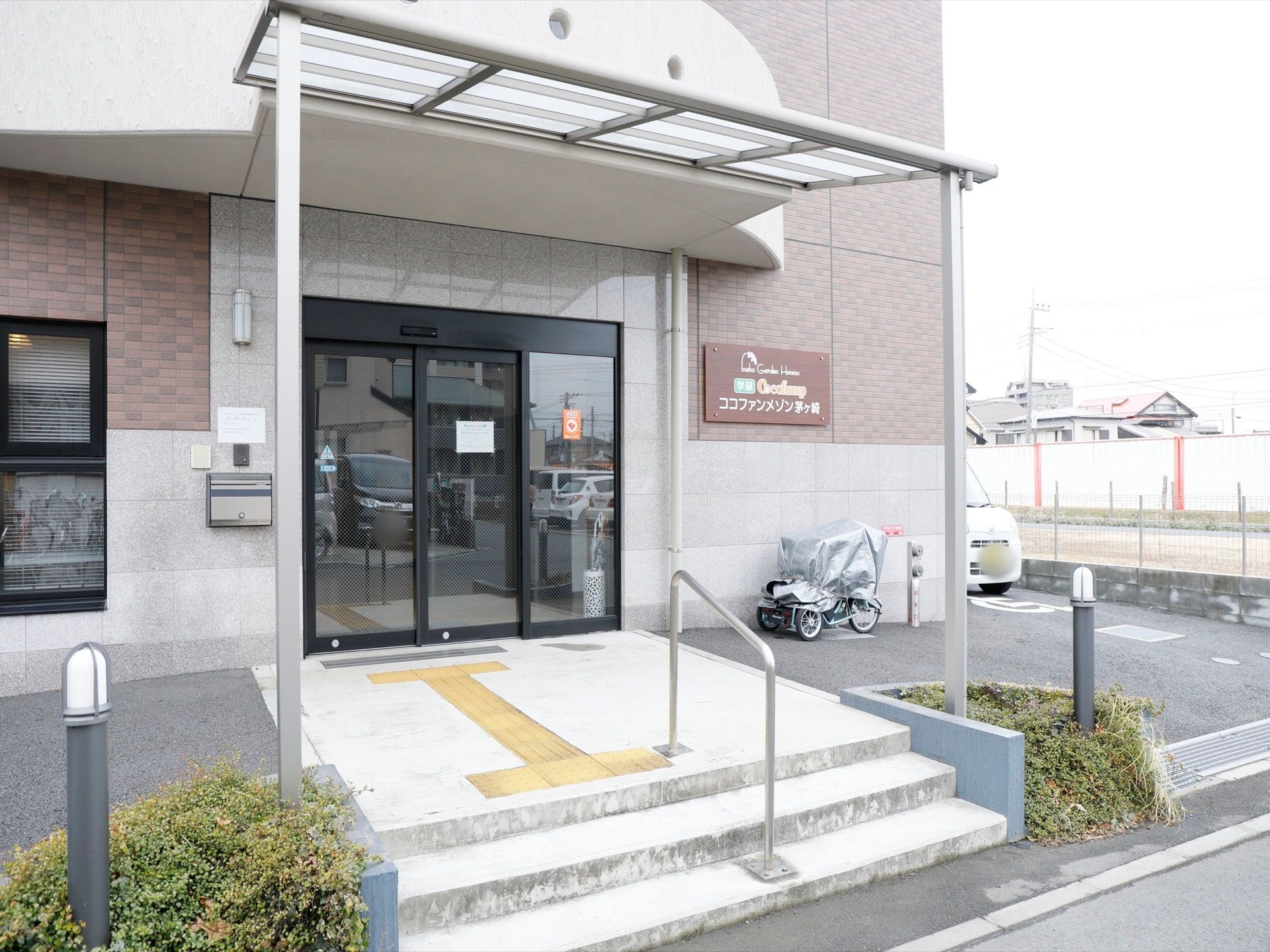 施設の入口前のスペースは大きな屋根が付いている。生活道路との間は3段程の階段があり、手すりが付いている。