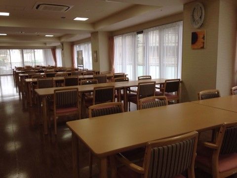 たくさん窓のある広々とした食堂である。４人掛けのダイニングテーブルとひじ掛け付きの椅子がたくさん配置されている。