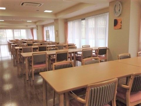 L字型に窓がある食堂にはダイニングテーブルが整然と並んでいる。たくさんの入居者様が一緒に食事ができる。